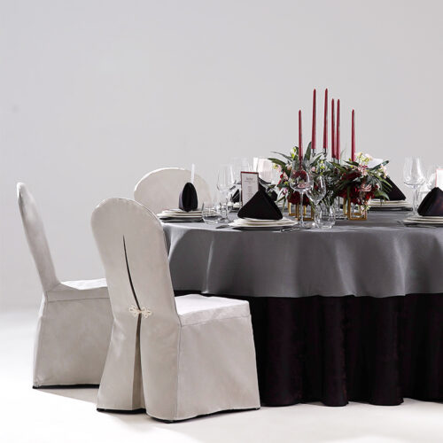 Round hotel banquet table styled with dark grey top tablecloth, black base skirt, black napkins, red candles, and silver-grey chair covers with frog buttons.