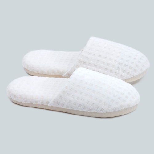Pair of white closed-toe hotel slippers with a raised grid pattern waffle texture and thick cushioned sole.
