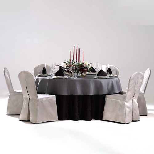 Round hotel banquet table styled with a charcoal top tablecloth, dark base skirt, center floral decor, and beige fitted chair covers.